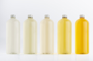 Assortment of plastic tall bottles with beverage of different pastel pale colors or cosmetic essential oil, silver cap mockup on white background, template.
