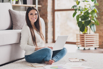 Full size photo of attractive happy positive good mood cheerful woman sit floor with crossed legs working in laptop at home