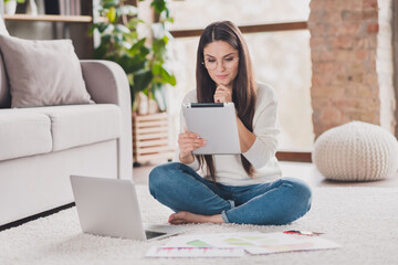 Photo of minded smart lady sit carpet laptop hold tablet finger chin wear eyeglasses white pullover...