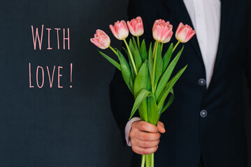 Man in a suit giving a bouquet of pink tulips. Greeting card with text with love