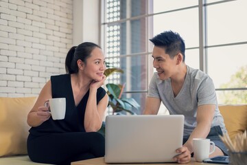 Asian man and woman family in casual outfit sitting in living room drinking coffee and using laptop together in happy and smile emotion