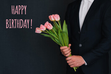 Bouquet of pink flowers of tulips in men's hands. Greeting card with the inscription Happy birthday