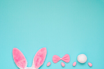 Easter holiday background with pink bunny ears, bow and pink eggs on a blue background