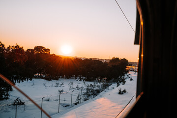 Beautiful snowy landscape from the train in the sunset. View of the snowy forest with the sunset light. Landscape of traveling by train in a snowy day in the sunset.