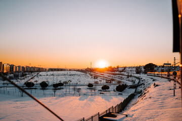 Obraz premium Beautiful view of the city with a lot of snow in the streets from the train while some buildings are illuminated by the sun. Concept of landscape of the snowy city at the sunset.
