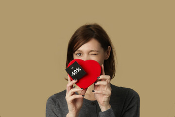 Portrait of young woman holds red heart shaped gift box with discount tag on it.
