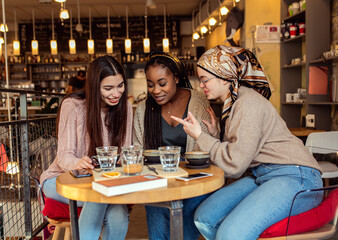Three young multi ethnic women enjoy coffee at a coffee shop.