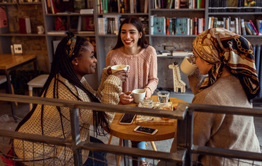 Three young multi ethnic women enjoy coffee at a coffee shop.