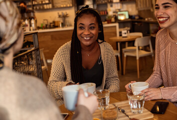 Three young multi ethnic women enjoy coffee at a coffee shop.