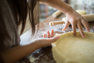Girl's hands preparing a tart crust, pressing the dough with her finger to fit the pastry to the tart pan