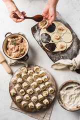 Women's hands sculpt dumplings. A lot of ready to cook pork dumplings on a large wooden board with flour.