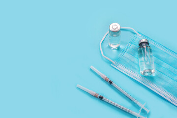 Vaccines and syringes, face mask on blue background.