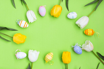 Fototapeta na wymiar Color easter eggs and White yellow tulips on a green background.