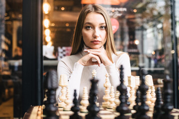Beautiful girl play chess, queen’s gambit play and everyone wins, a smart and pensive face. White and black chess pieces are displayed on the board. mental game, a lot of time to last, not for fools