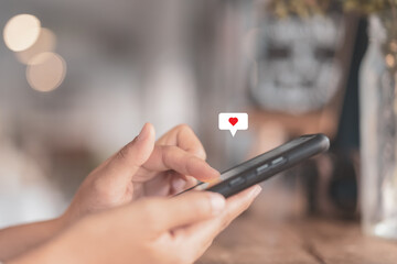 Woman hand using smartphone with heart icon at coffee shop background. Technology business and social lifestyle concept.