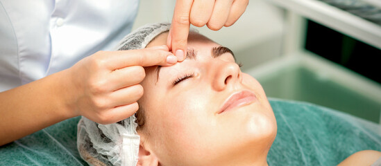 Beautician's hands make massage on eyebrow for a woman while a facial massage in cosmetology clinic center