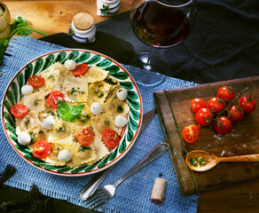 Ravioli with pesto sauce garnished with parmesan cheese and basil, tomatoes and mozzarella on table near glass of wine. Italian dinner concept.