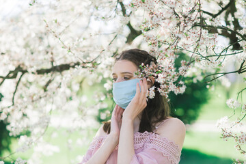 A girl in protective medical mask in spring among the blooming garden. Spring allergy conception