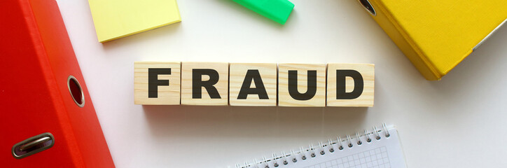 Wooden cubes with word FRAUD on the office desk. Folder and other office supplies.