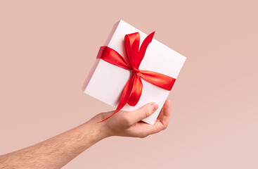 Romantic gift box banner. Online shopping for Valentines Day 2021. Delivery poster. Man hold a gift box wrapped in red ribbon and bow on natural colored background. Trendy style greeting card. Sale ad