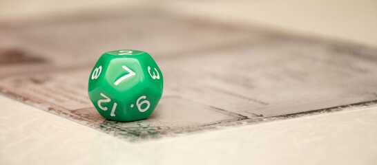 A multi faceted green D12 cube lies on the game map of the board game at home and show 7, a banner with a place for text