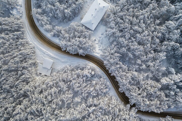 Top view with curvy mountain road in snow covered forest.