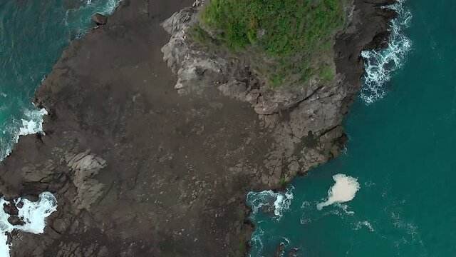 Cinematic aerial footage rock beach top down view from drone flying trucking shot showing foamy sea wave splashing to the rock pavement