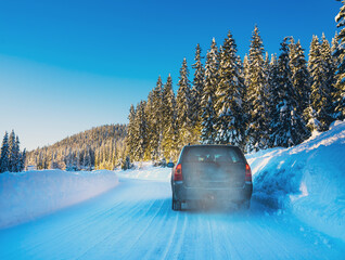 Car driving on a snow covered road in a wilderness forest on a bright sunny winters day.
