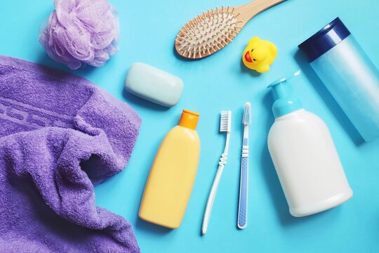Flat lay composition bath products on a blue background. Purple towel, shampoo bottle, sponge, soap bar, shower gel, hair balm, comb, toothbrushes and rubber duck. Toiletries set