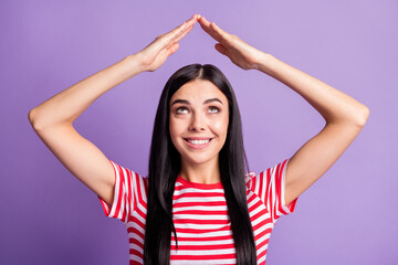 Fototapeta na wymiar Photo of funny young girl hold arms roof look up empty space wear striped red shirt isolated purple color background
