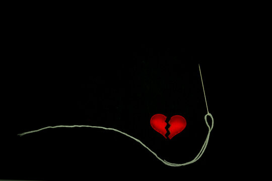Healing broken heart concept, red heart is sewn with  white thread with needle on black background