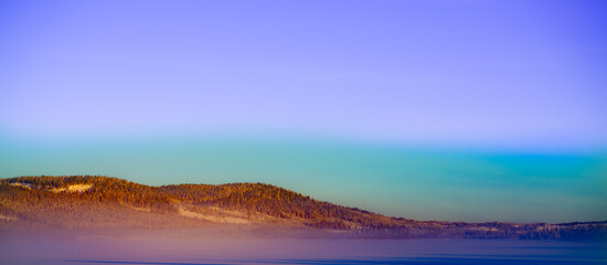 Beautiful snowy winter panorama over a frozen lake covered in heavy snow and a frozen haze hanging low in a colorful evening sky.