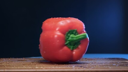 Ripe red bell pepper with thick peduncle rotates shaking small water drops on brown wooden board slow motion extreme closeup - Powered by Adobe