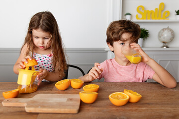Little girl juicing oranges while brother drinks freshly squized orange juice