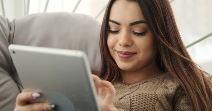 Happy woman using digital tablet sitting on luxury chair at home