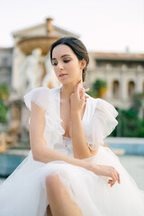 Naklejka premium Portrait of Beautiful bride in white fashion wedding dress. Outdoor romantic portrait of attractive brunette woman with hairstyle posing by fountain at park.
