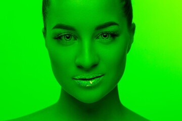 Make up. Handsome woman's portrait isolated on green studio background in neon light, monochrome. Beautiful female model. Concept of human emotions, facial expression, sales, ad, fashion and beauty.