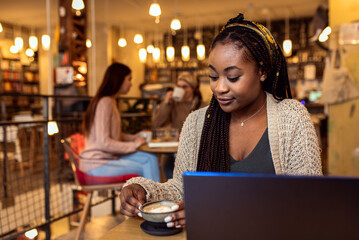 Portrait of young African woman using laptop in coffee shop.