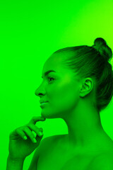 Well-kept. Handsome woman's portrait isolated on green studio background in neon light, monochrome. Beautiful female model. Concept of human emotions, facial expression, sales, ad, fashion and beauty.
