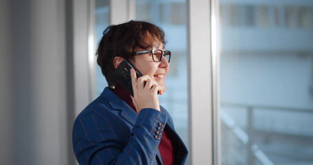 Asian young businessman wearing fashion suit talking on mobile phone in modern office near window