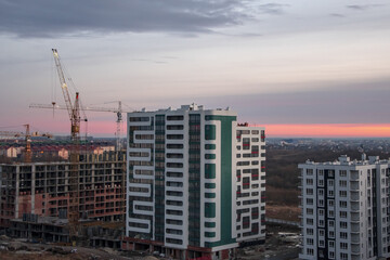 Fototapeta na wymiar modern multi-apartment high-rise building under construction on the background of construction cranes and the evening sunset sky.