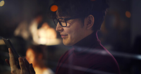 Asian office worker using smartphone standing near window in office late at night.