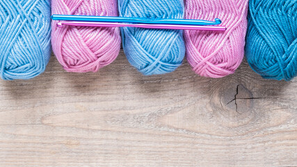 Multicolored crochet hooks with balls of yarn on a wooden background with copy space.