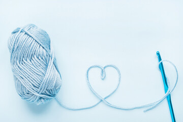 Crochet heart, hook and ball of yarn on a blue background with copy space.