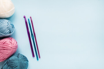 Multicolored crochet hooks with balls of yarn on a blue background with copy space.