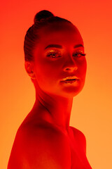 Fire. Handsome woman's portrait isolated on orange studio background in neon light, monochrome. Beautiful female model. Concept of human emotions, facial expression, sales, ad, fashion and beauty.