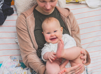 Cheerful baby with one tooth sits on her mother's lap