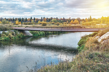 Empty bridge made of old metal pipes with small railing over tranquil river at rural site in nice summer evening close view