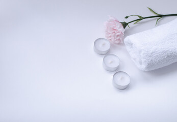 white, terry towel with a pink flower on top and candles on a white background
