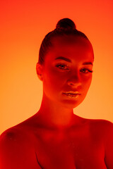 Evening. Handsome woman's portrait isolated on orange studio background in neon light, monochrome. Beautiful female model. Concept of human emotions, facial expression, sales, ad, fashion and beauty.